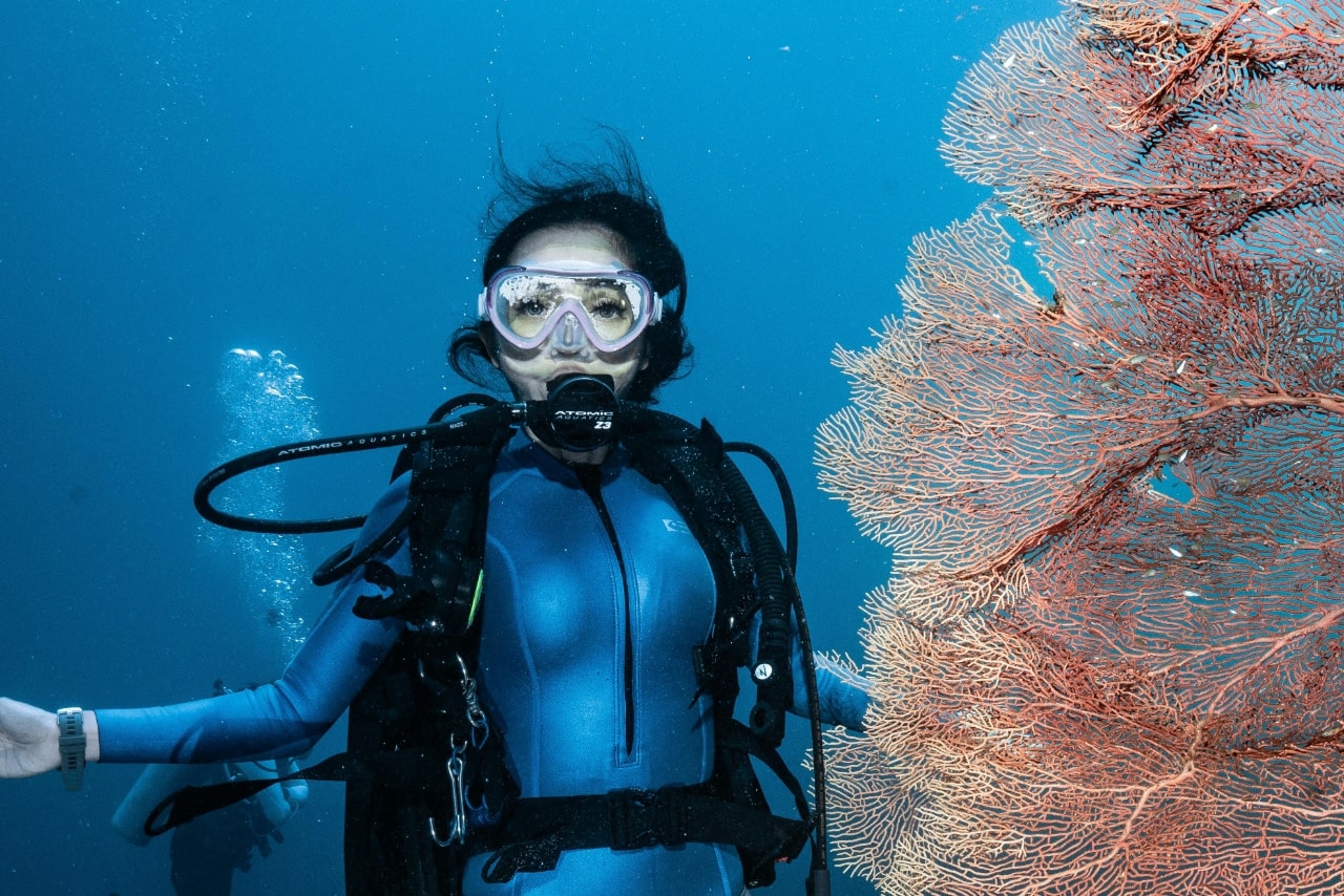 A woman deep sea scuba diving next to coral while wearing a divers watch