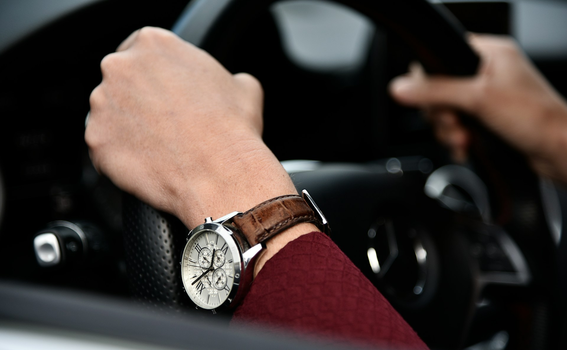 a close-up of a pair of hands holding a steering wheel wearing a chronograph watch