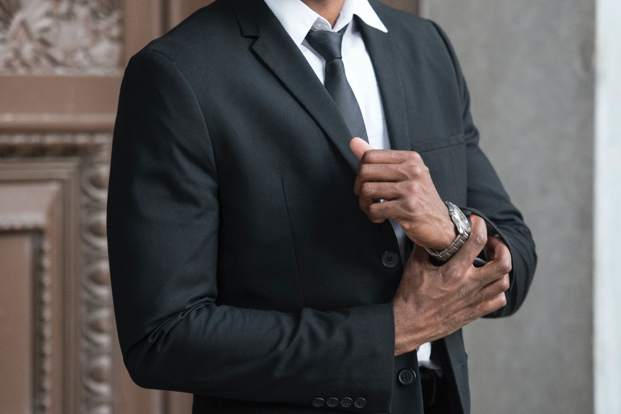 A man wearing an all black suit while wearing a stainless steel watch.