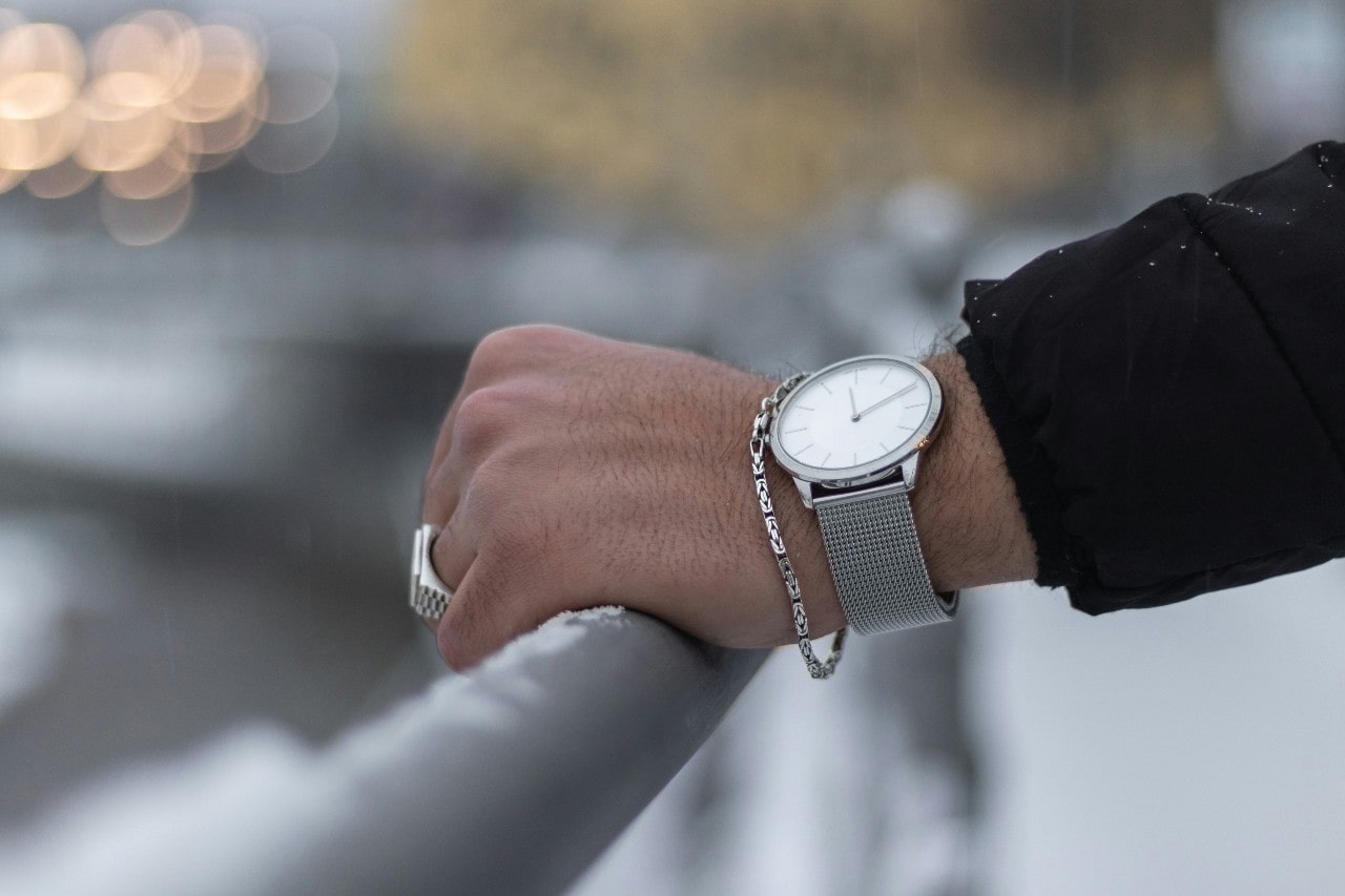 a man’s hand resting on a metal rail wearing a white and silver luxury watch