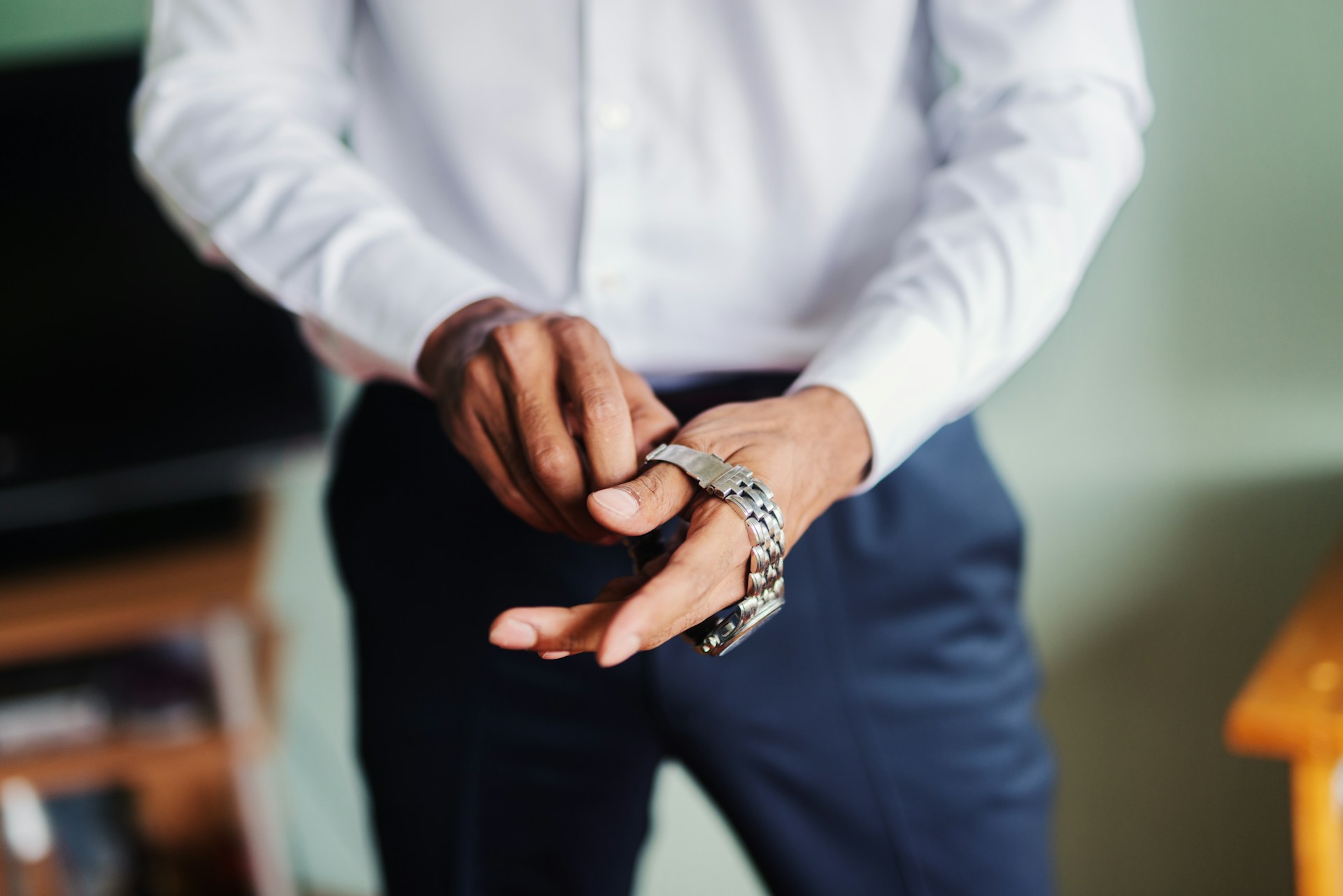 a man putting on a fine silver watch and wearing suit pants