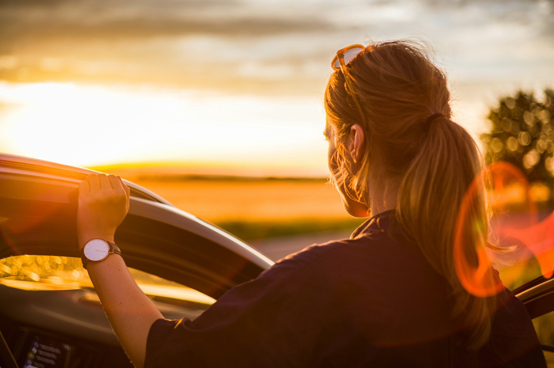 a woman standing next to an open car door, wearing a white and gold watch