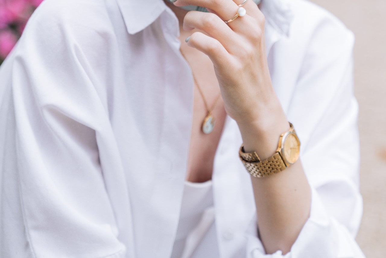 a woman raising her hand to her chin and wearing a monochrome yellow gold watch