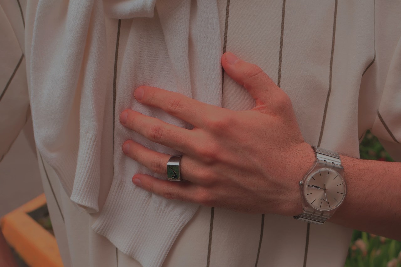 a man’s hand resting on his chest, wearing a silver ring and wristwatch