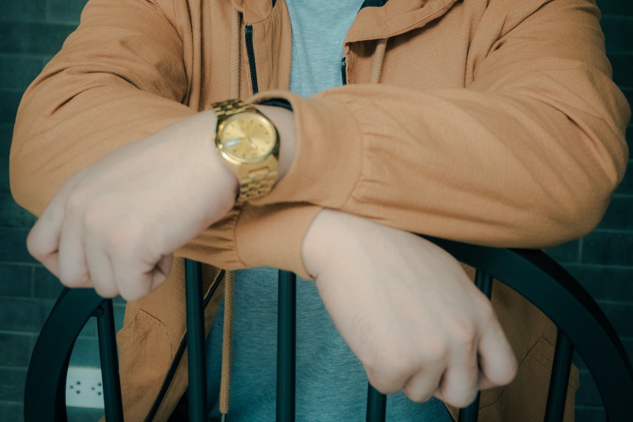 a man leaning on the back of a chair wearing a monochrome yellow gold watch