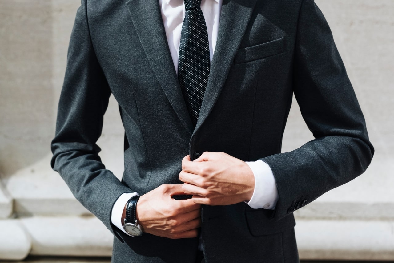 a man buttoning his suit while wearing a watch with a black leather band and a silver dial.