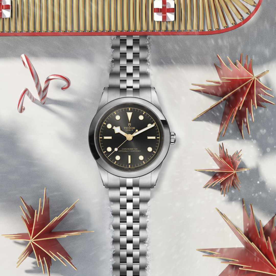 A close-up of a TUDOR Black Bay 41 watch displayed below a conveyor belt with gifts on a festive backdrop.