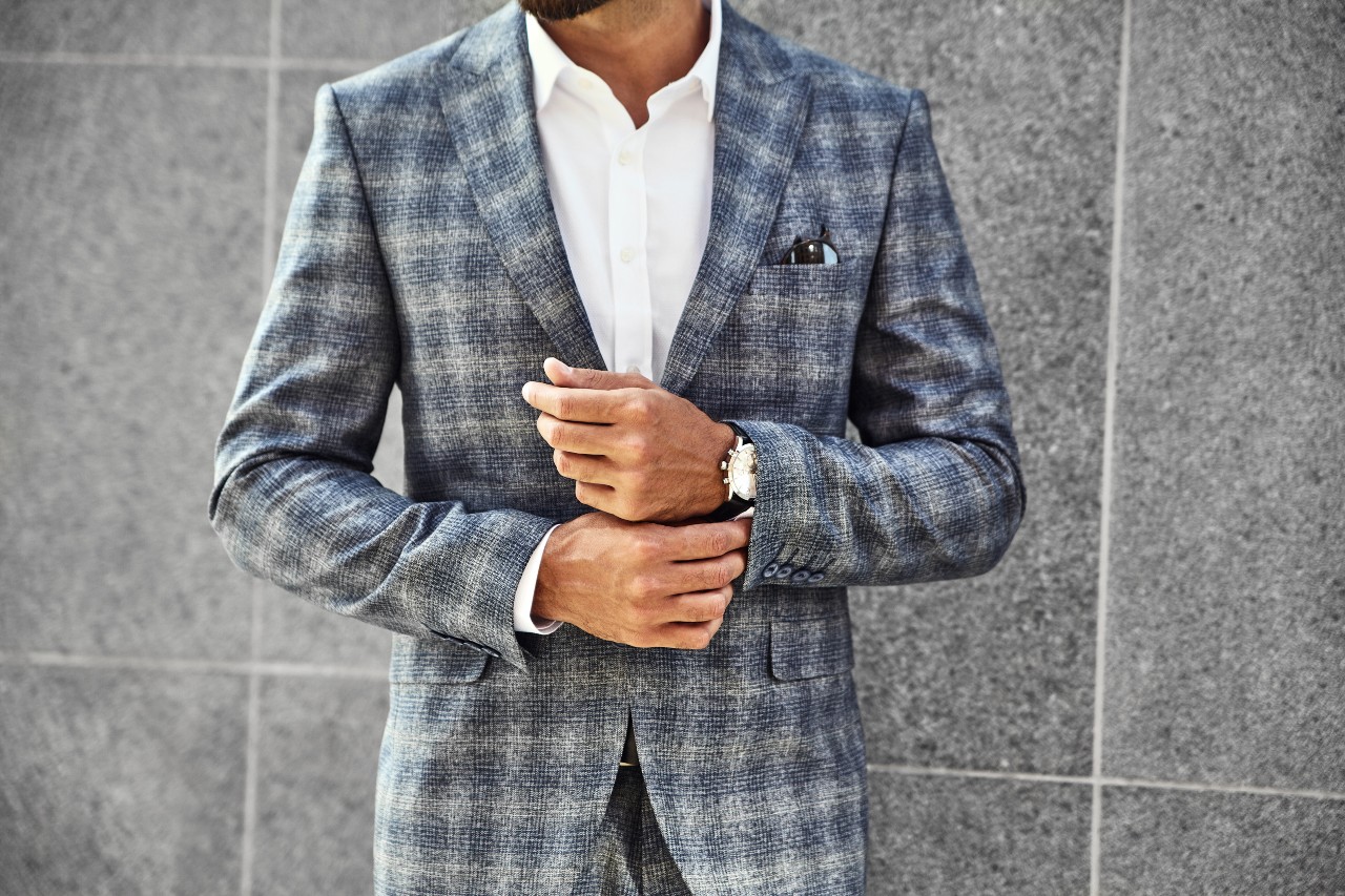 A man adjusting his watch band in a plaid suit