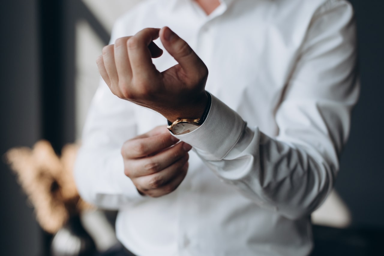 A man in a dress shirt adjusting his cuff over his luxury dress watch