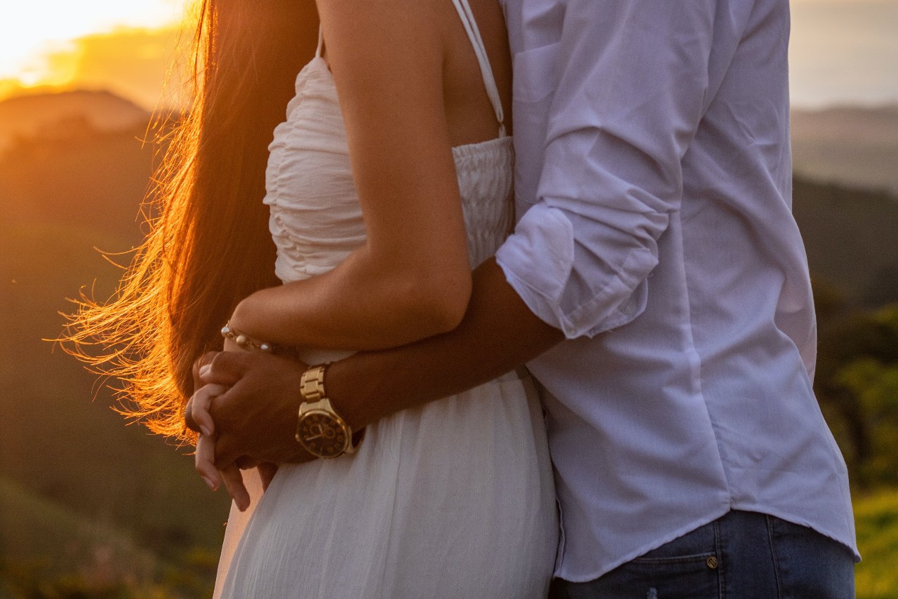 A man and woman hugging at sunset while wearing a gold toned watch