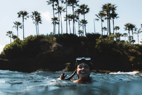 a woman swimming in the ocean in front of palm trees, wearing a snorkel and goggles 