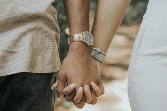 A couple holding hands, the man wearing a yellow gold luxury watch.