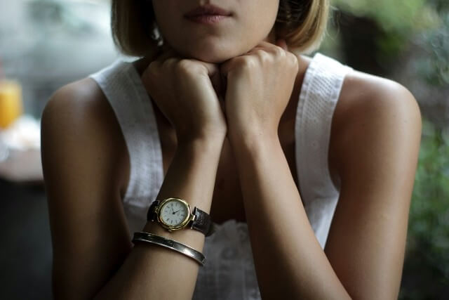 A woman with her chin resting on her hands, wearing a yellow gold luxury watch.