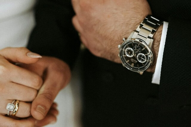 a bride and groom holding hands – the groom wearing a silver watch with a black dial