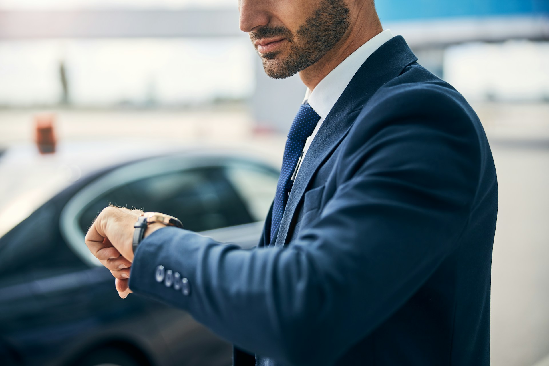 a man in a suit looking down at his gold watch with a black leather strap