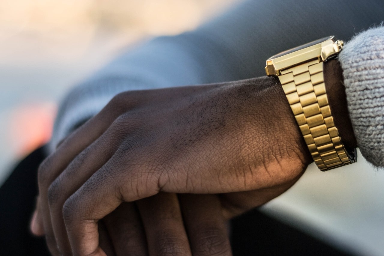 A close up side view of a man’s hand and his yellow gold watch he is wearing with a light gray sweater