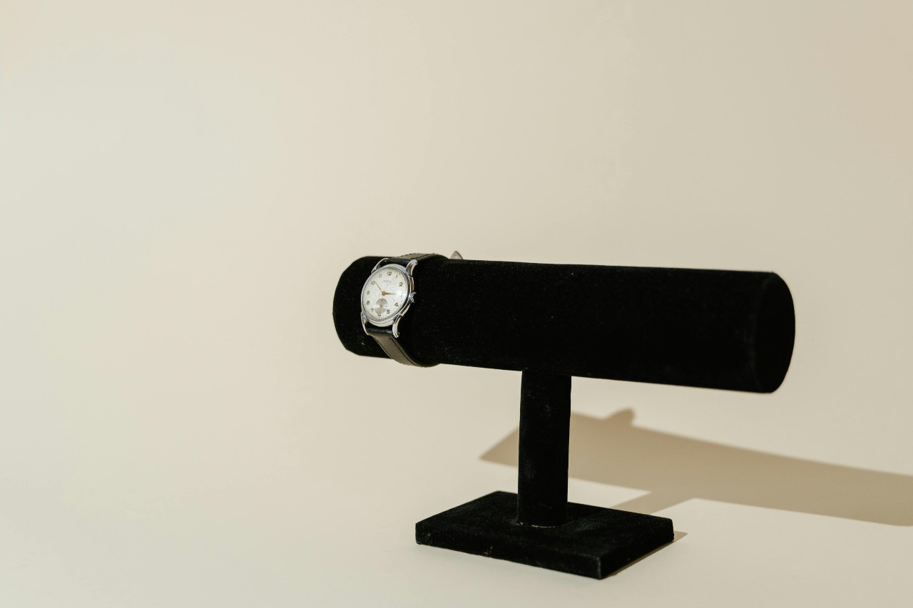 a silver watch with black strap on a black velvet watch stand