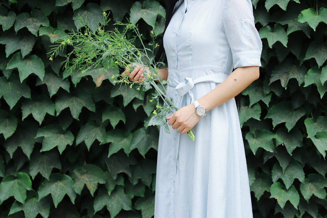 a woman in a blue dress holding greenery and wearing a white watch