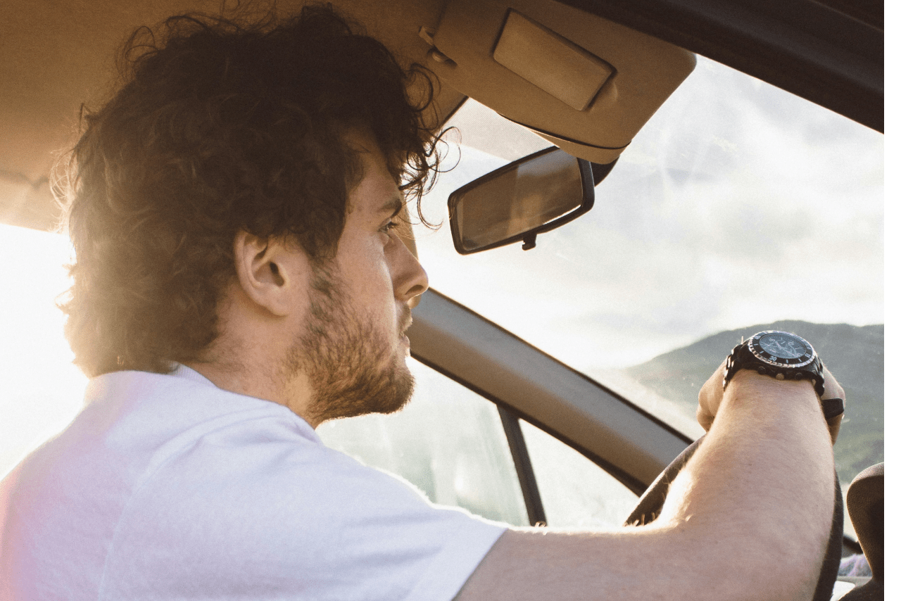 a man driving a car and resting his arm on the wheel, adorned with a black watch